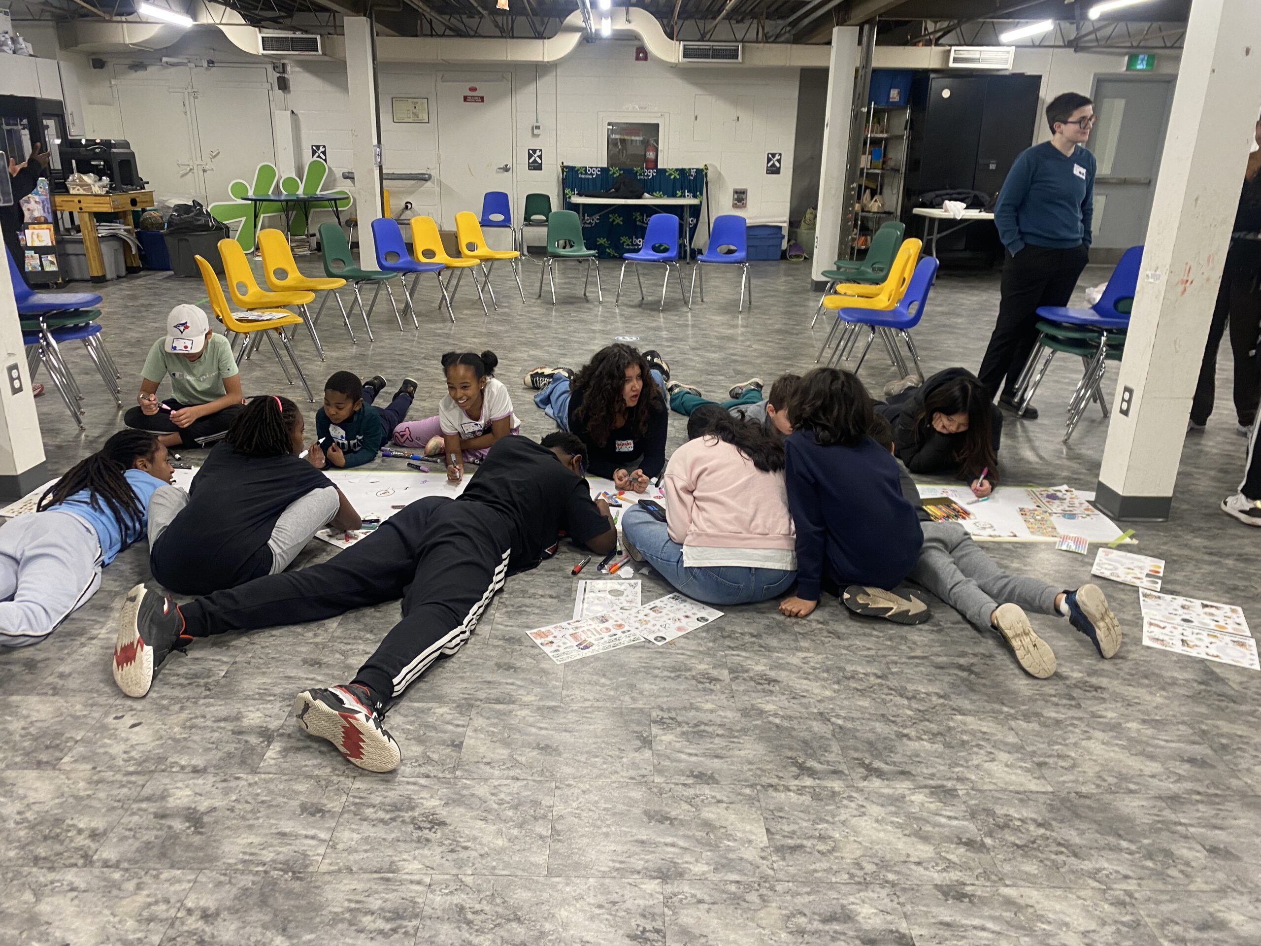 A group of youth scattered out on the floor drawing on paper and being creative in a group setting.