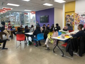 Large group of youth sitting in brightly-coloured chairs facing away from camera