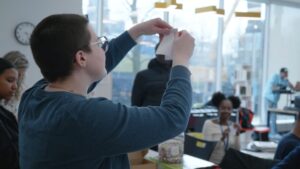 Youth with glasses holding piece of paper up using two hands.