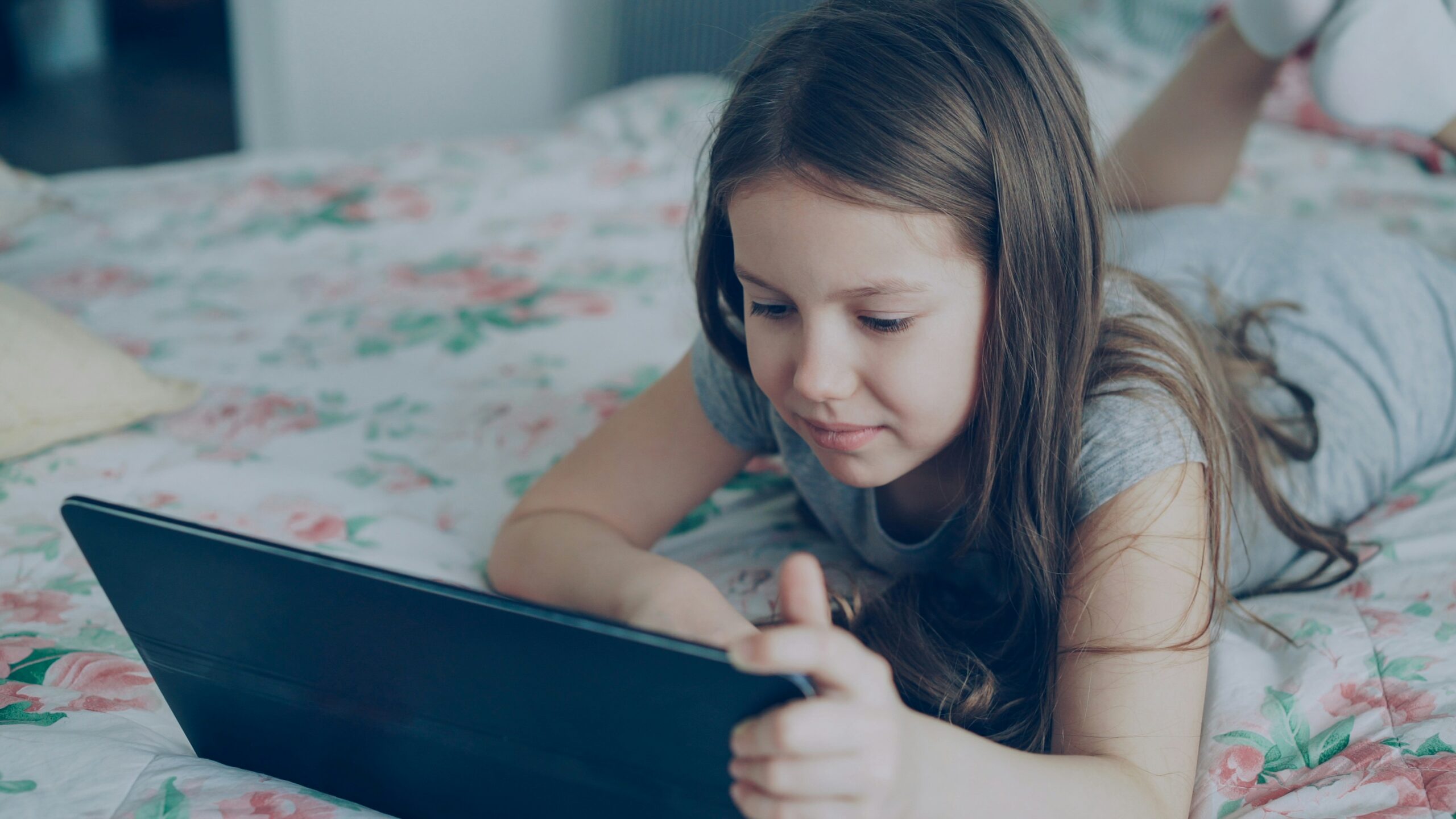 Young girl around 10 years old staring at a tablet screen in bed.